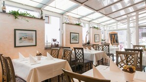 Restaurante com mesas postas para refeições, obras de arte nas paredes e teto de vidro.