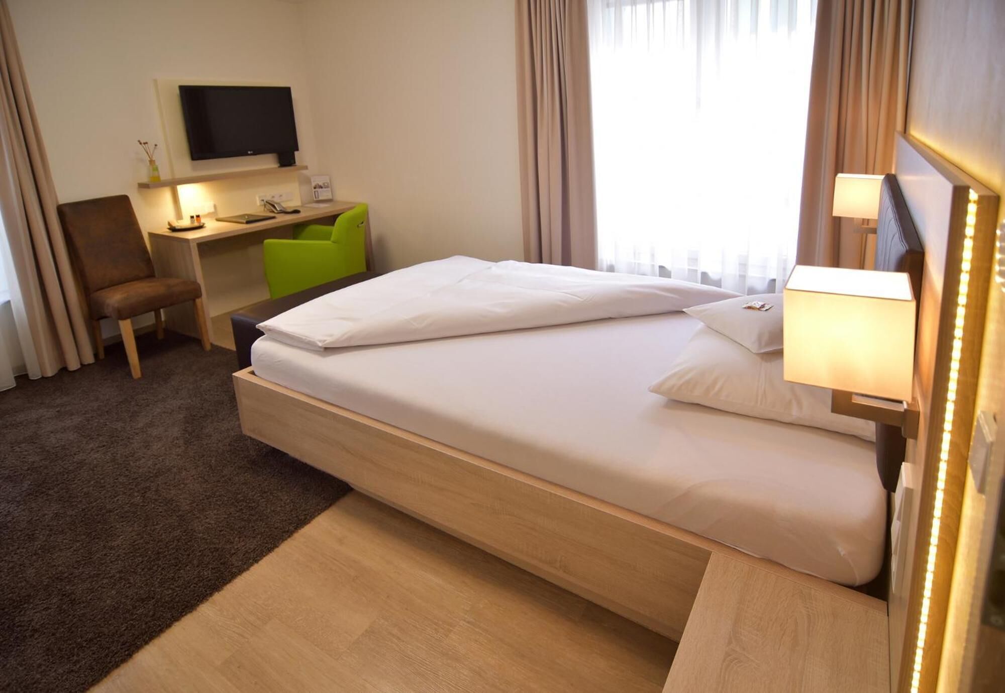 A hotel room with a bed, a desk, a chair, a television, and a lamp.