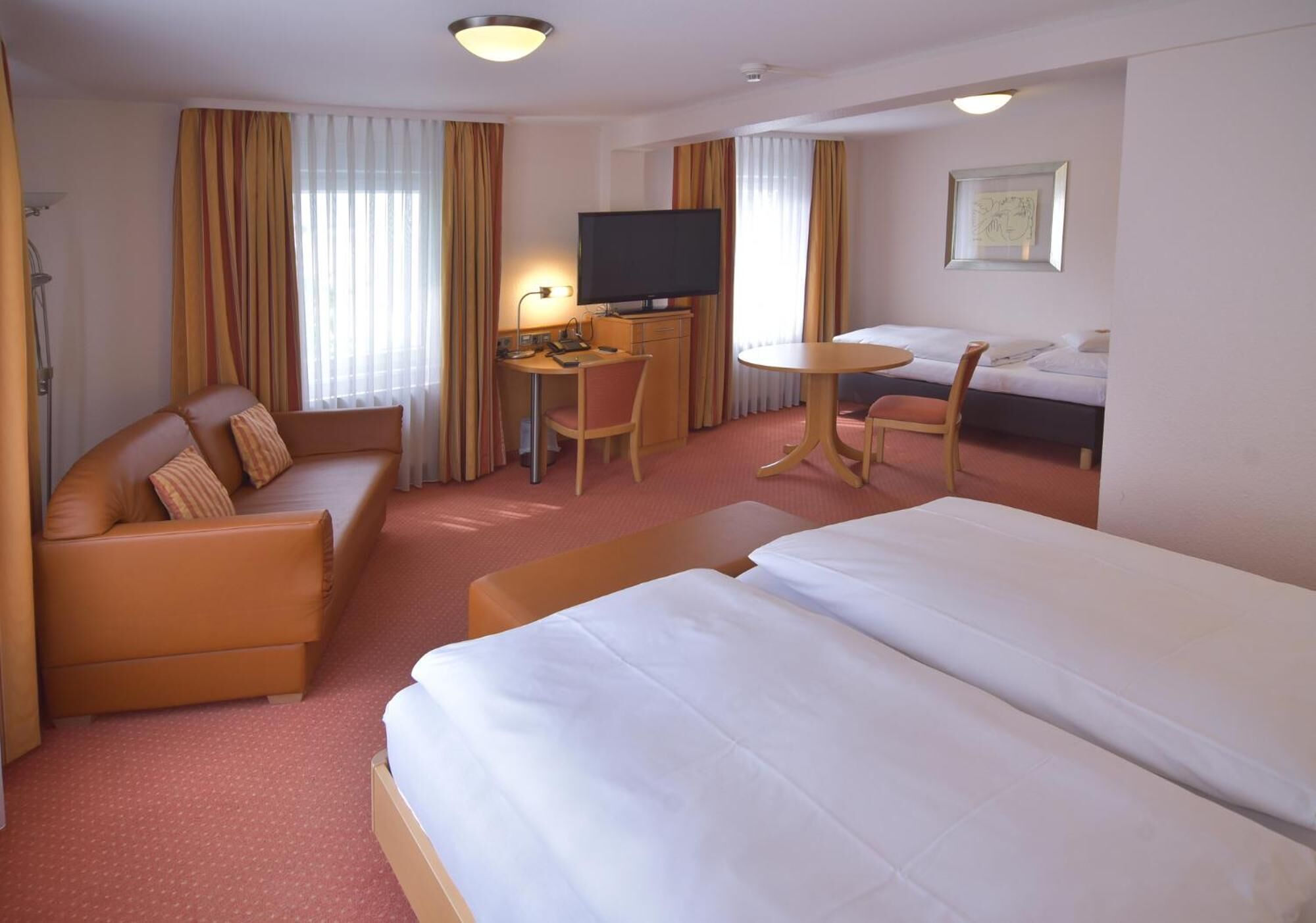 A hotel room with a bed, a sofa, a desk with a TV, and a small table.