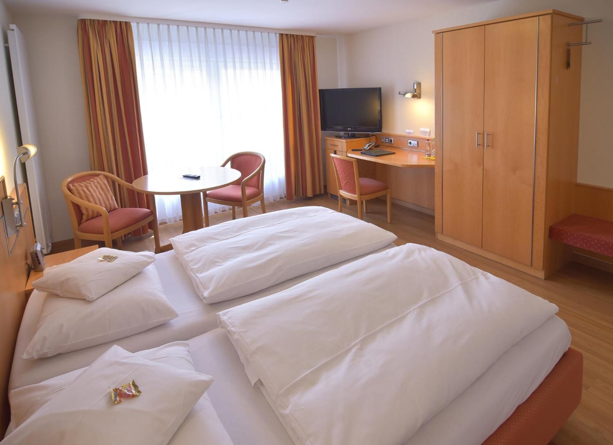 A hotel room with two beds, a desk, a television, and a wardrobe.