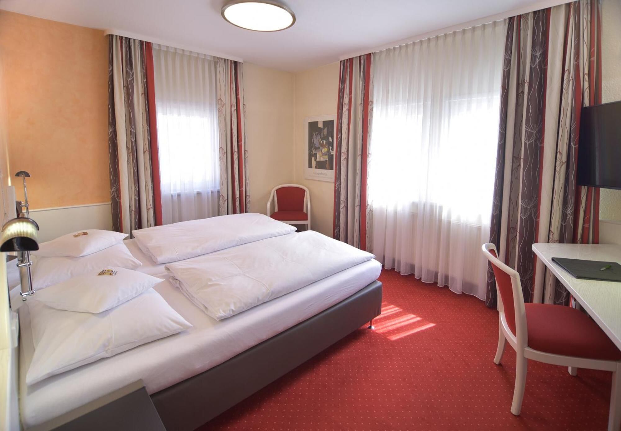 A hotel room with a bed, a desk, a chair, a TV, and curtains.