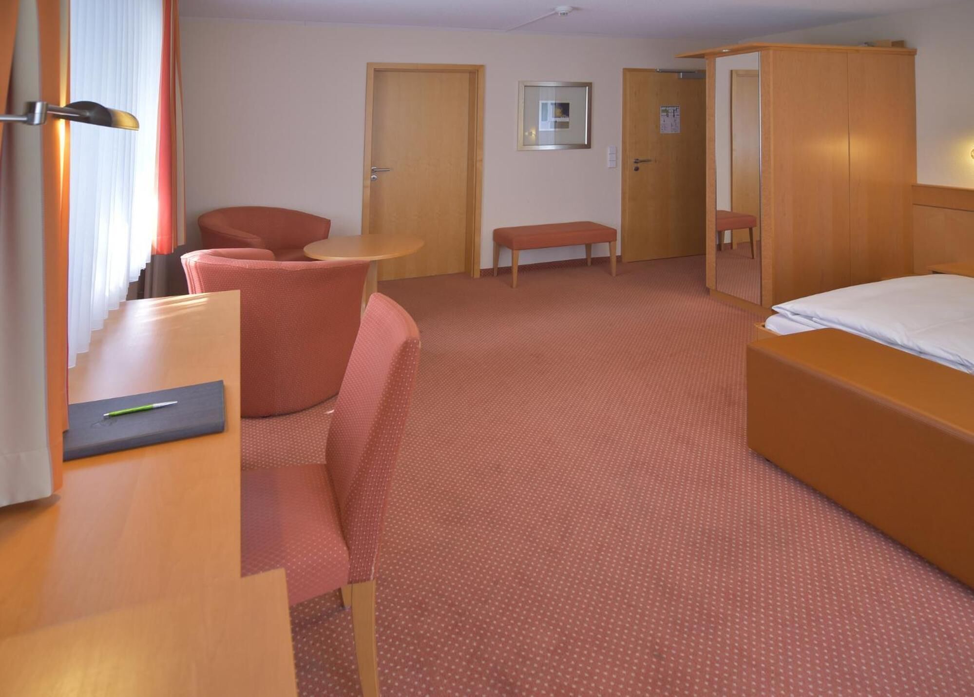 Ein Hotelzimmer mit einem Bett, einem Schreibtisch mit Stuhl, einem kleinen Tisch und einer Bank.