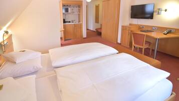 A hotel room with two beds, a desk, a television, and a kitchenette.