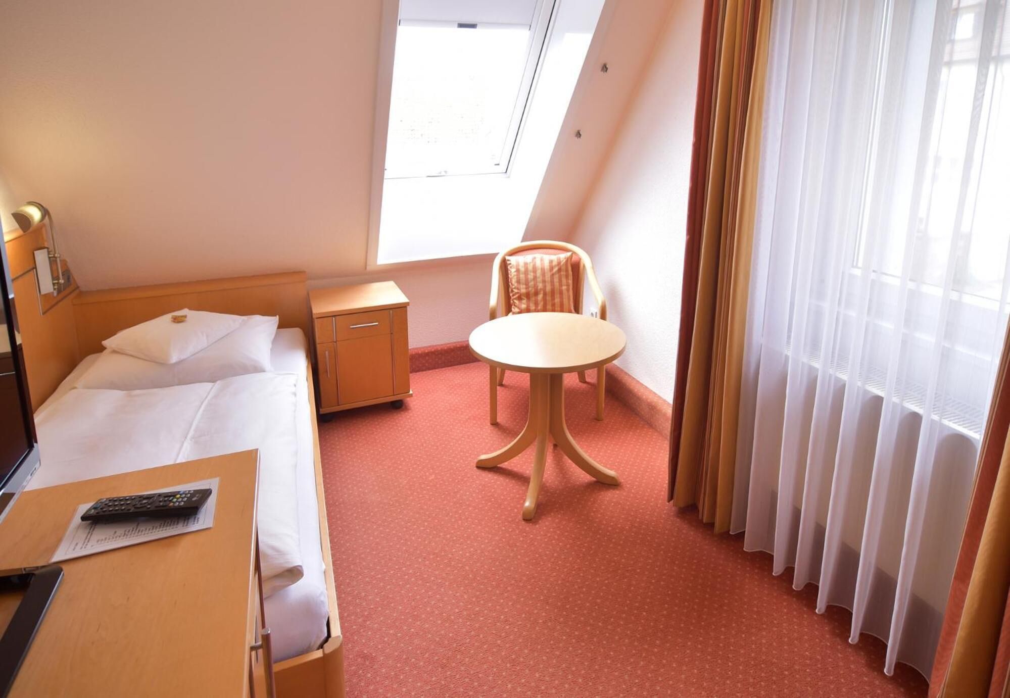 A hotel room with a bed, a desk, a chair, a small table, and a window with curtains.