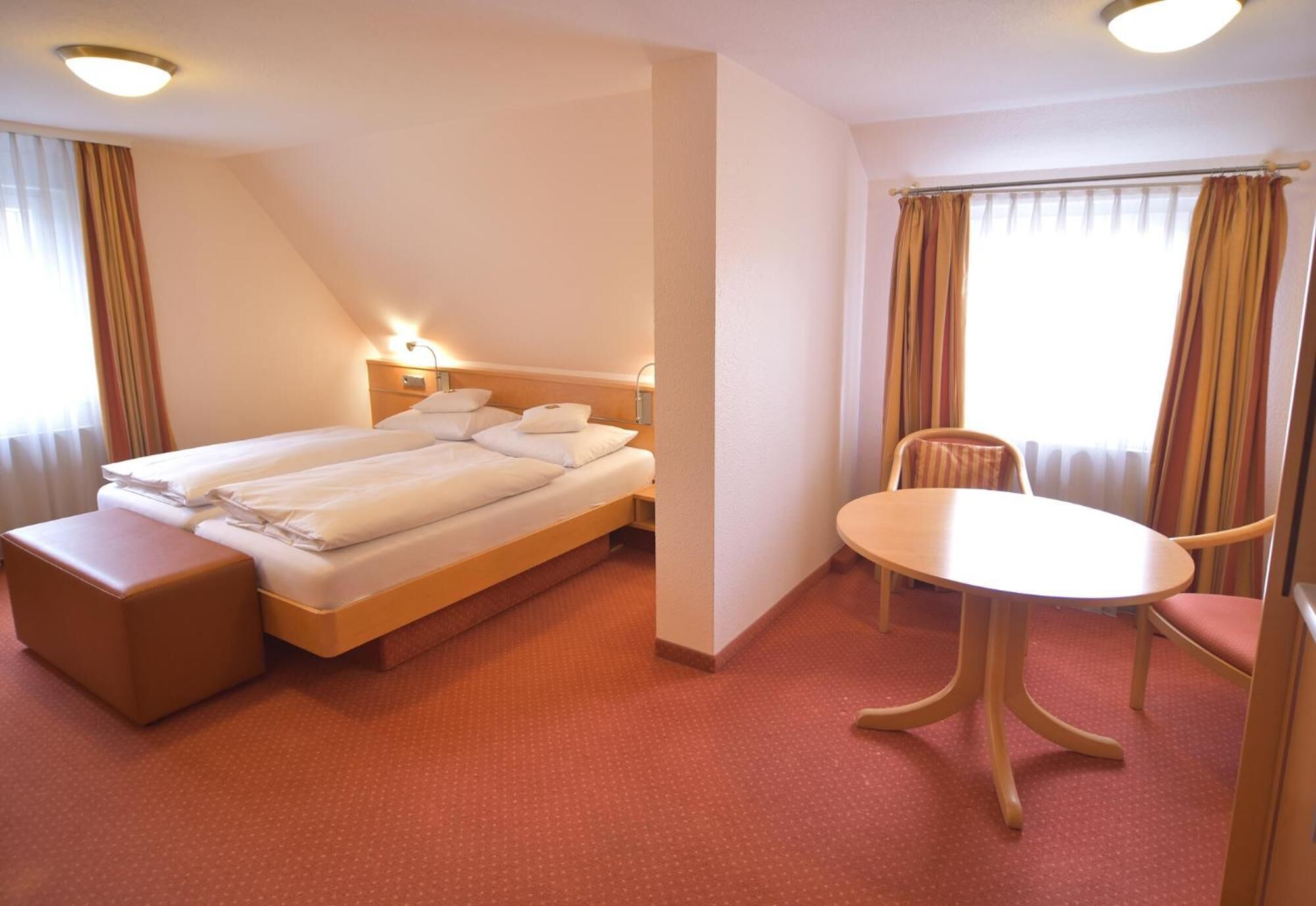 Una habitación de hotel con una cama, una mesita de noche, una silla y una ventana con cortinas.