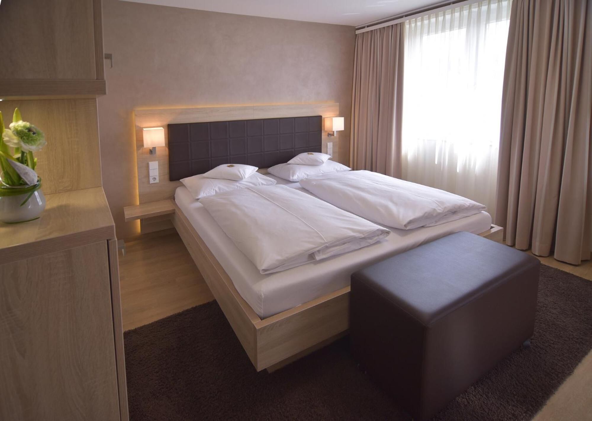 Et hotelværelse med en seng, sengeborde, en lampe og et gardinforhængt vindue med en potteplante.