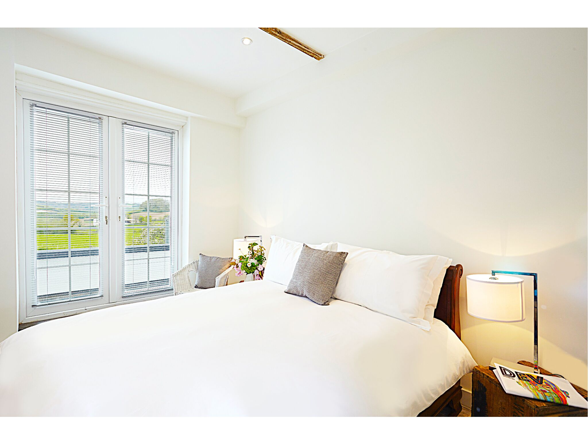 A bedroom with a large bed, a nightstand with a lamp, and a window with blinds.
