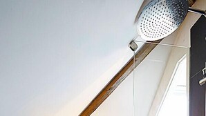 A modern bathroom with a sloped ceiling, a shower, a toilet, and a sink area with toiletries.
