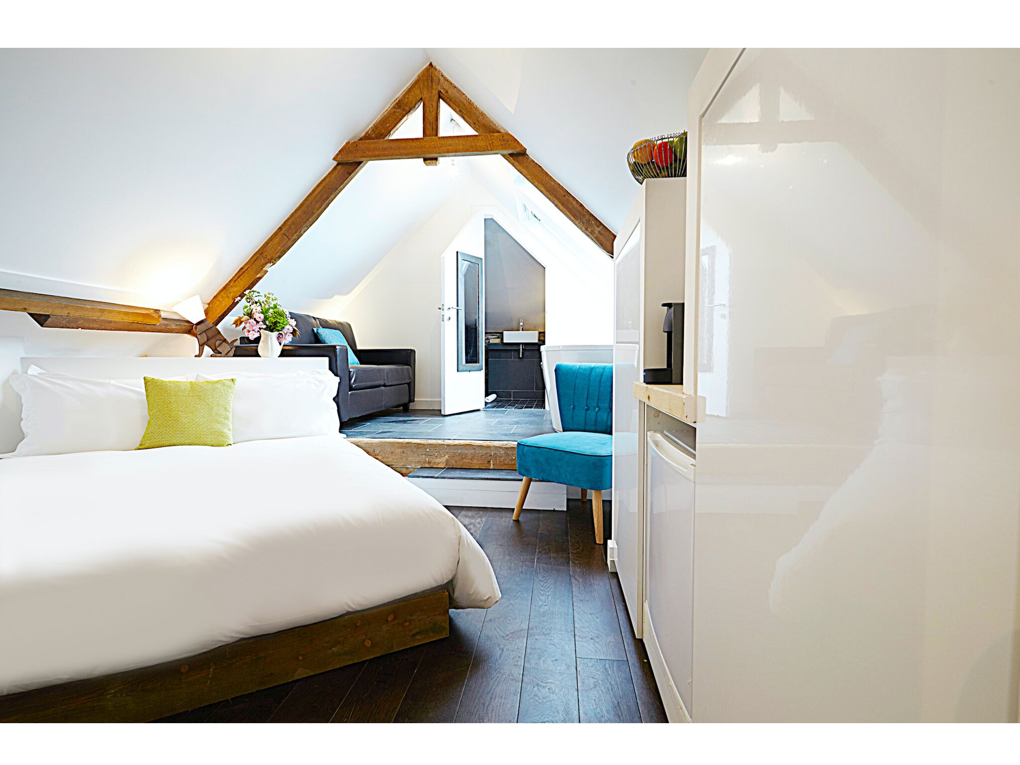 A bedroom with a large bed, a blue chair, and a kitchenette area.
