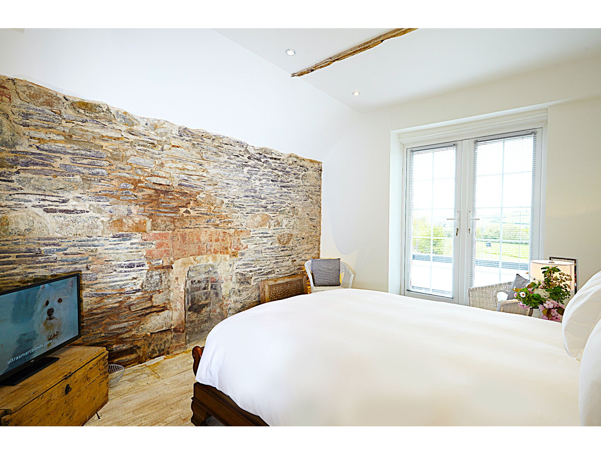 Un dormitorio con pared de piedra, una cama, un ventanal y una mesita de noche con un marco de fotos.