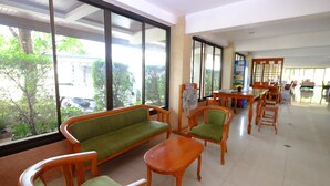 A spacious room with large windows, a sofa, chairs, and a small table. - PC Palace Hotel (Sakon Nakhon)