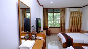 A hotel room with a wooden desk, a television, a telephone, a bed with a patterned bedspread, and a window with curtains. - PC Palace Hotel (Sakon Nakhon)