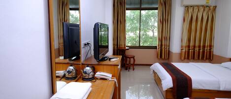 Habitación de hotel con escritorio de madera, televisor, teléfono, cama con colcha estampada y ventana con cortinas.