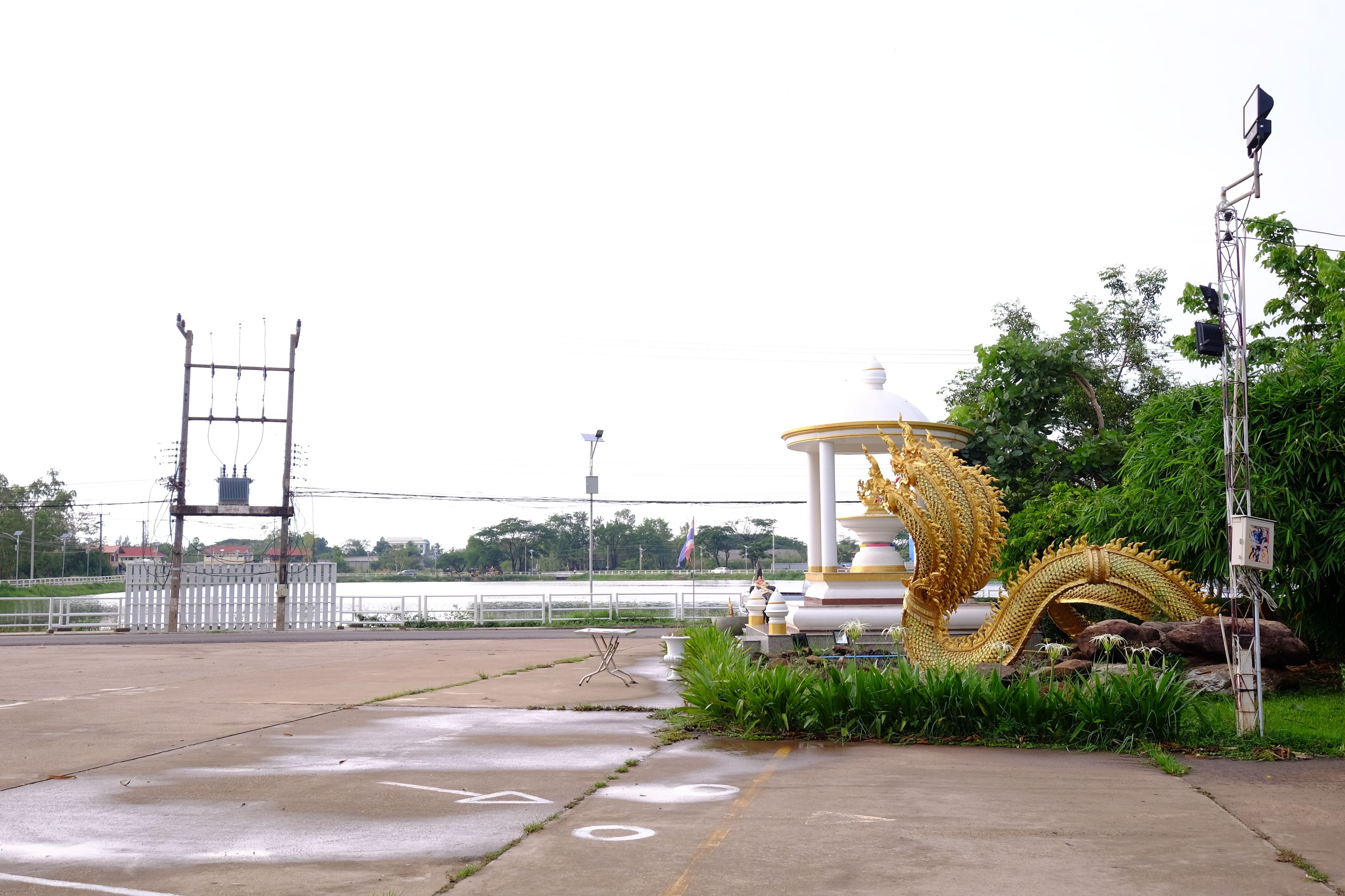 Un parc avec une grande statue de dragon doré, un kiosque blanc et un pont en arrière-plan.