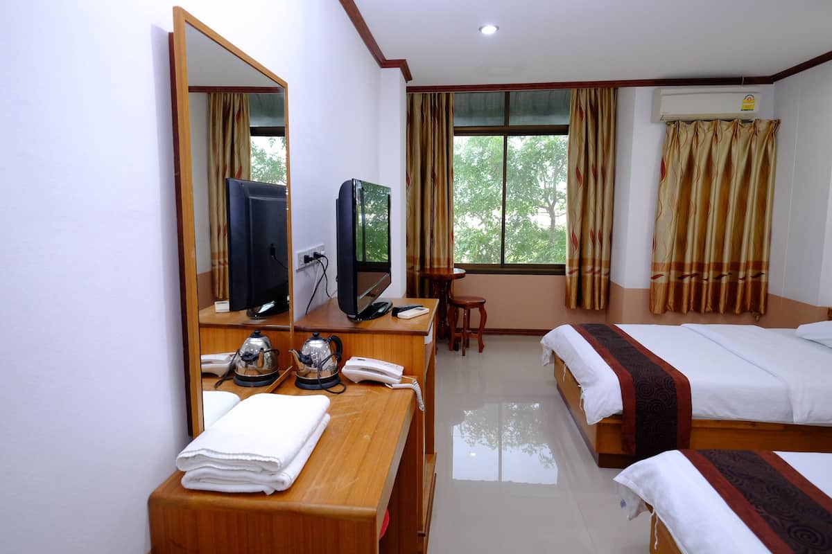 A hotel room with a wooden desk, a television, a telephone, a bed, and a window with curtains.