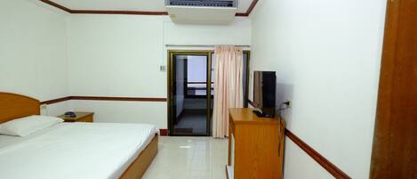 A hotel room with a bed, a wooden nightstand, a television, and an air conditioning unit.
