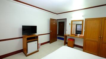 A hotel room with a bed, a television on a wooden stand, a small refrigerator, a wooden wardrobe, a mirror, and a door leading to another room.