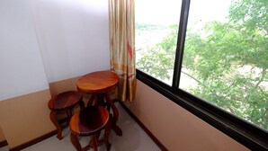 A corner room with a small wooden table and two chairs, a window with a view of greenery outside. - PC Palace Hotel (Sakon Nakhon)