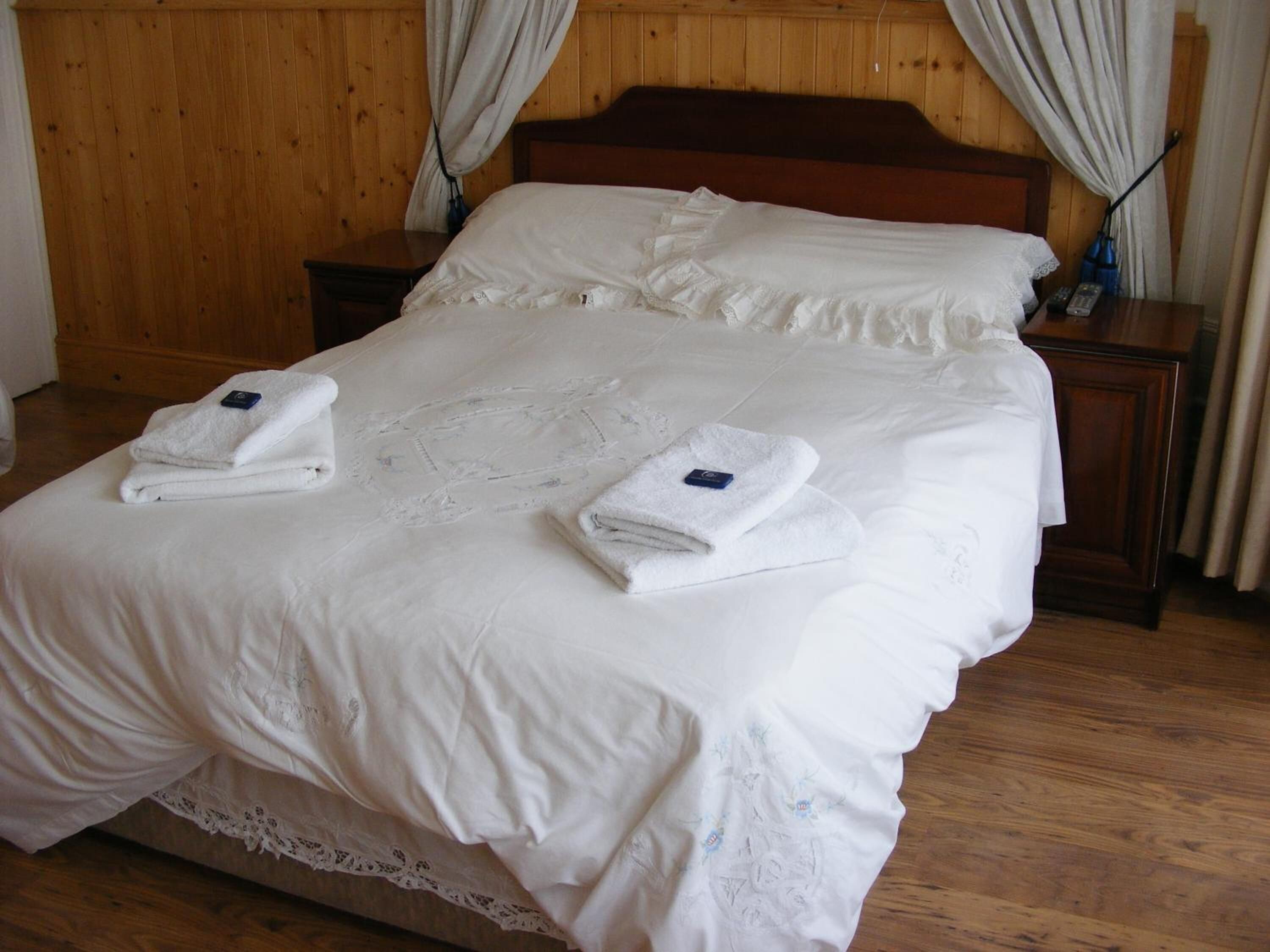 Una cama bien tendida con sábanas y toallas blancas, cabecera de madera y suelo de madera.