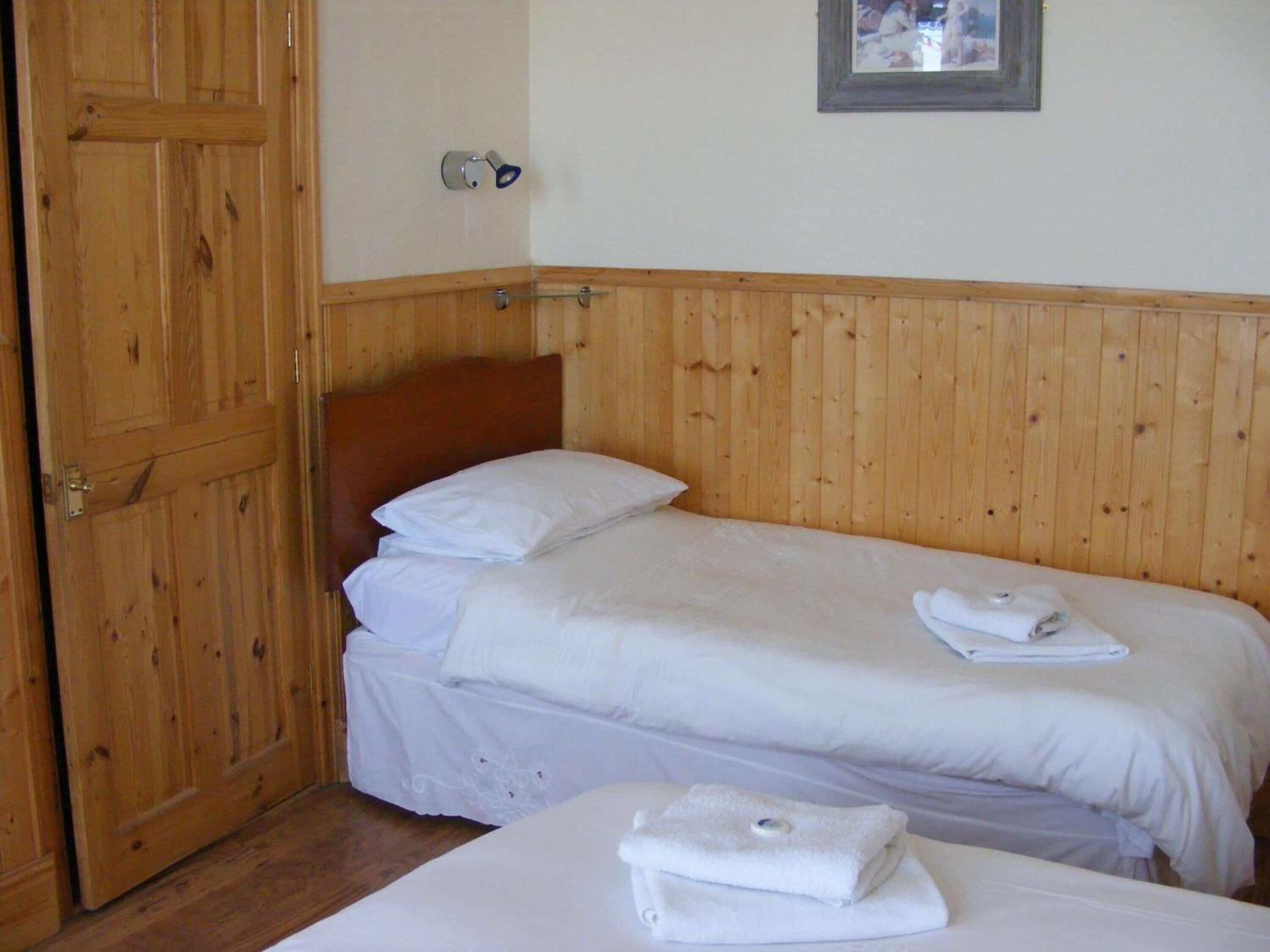 Une chambre avec deux lits simples, des lambris en bois sur les murs, une porte en bois et un tableau encadré accroché au mur.