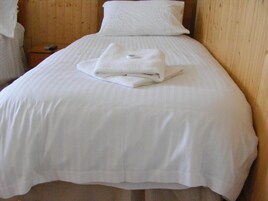 Una cama bien hecha con una toalla blanca doblada y una almohada sobre un cabecero de madera.