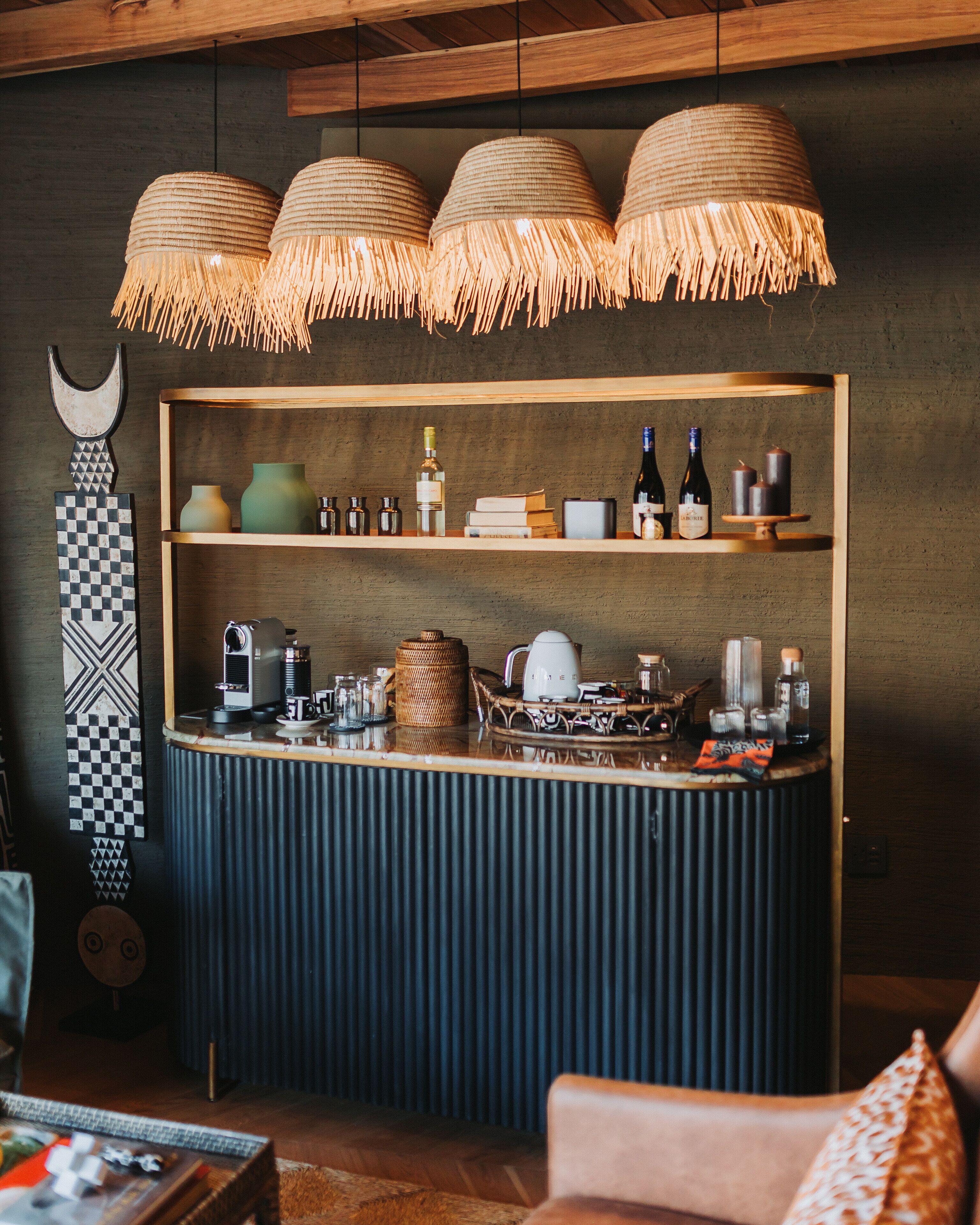 A bar area with a wooden counter, shelves with bottles and glasses, and hanging rattan lamps.