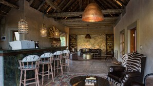 Een rustiek interieur met een bar, houten stoelen, een kamerbreed tapijt en een grote hanglamp.