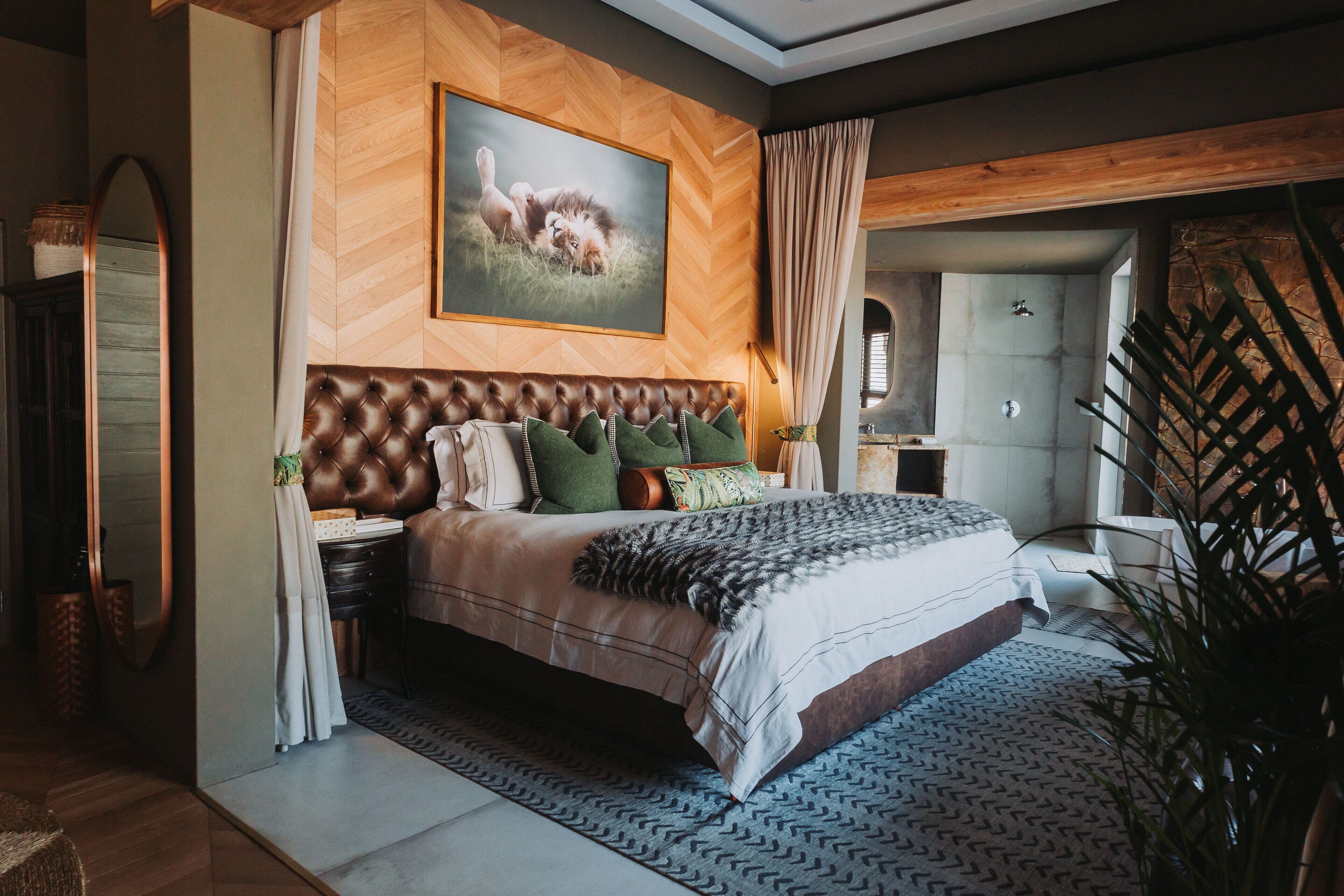 A bedroom with a large bed, a wooden headboard, a painting of a lioness, and a view of a bathroom.