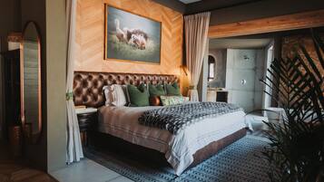 A bedroom with a large bed, a wooden headboard, a painting of a lioness, and a view of a bathroom.