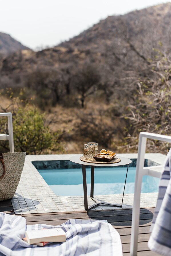 Un espace aménagé au bord de la piscine, avec une table où sont disposés des collations et des boissons, une chaise et un livre posé sur une couverture.