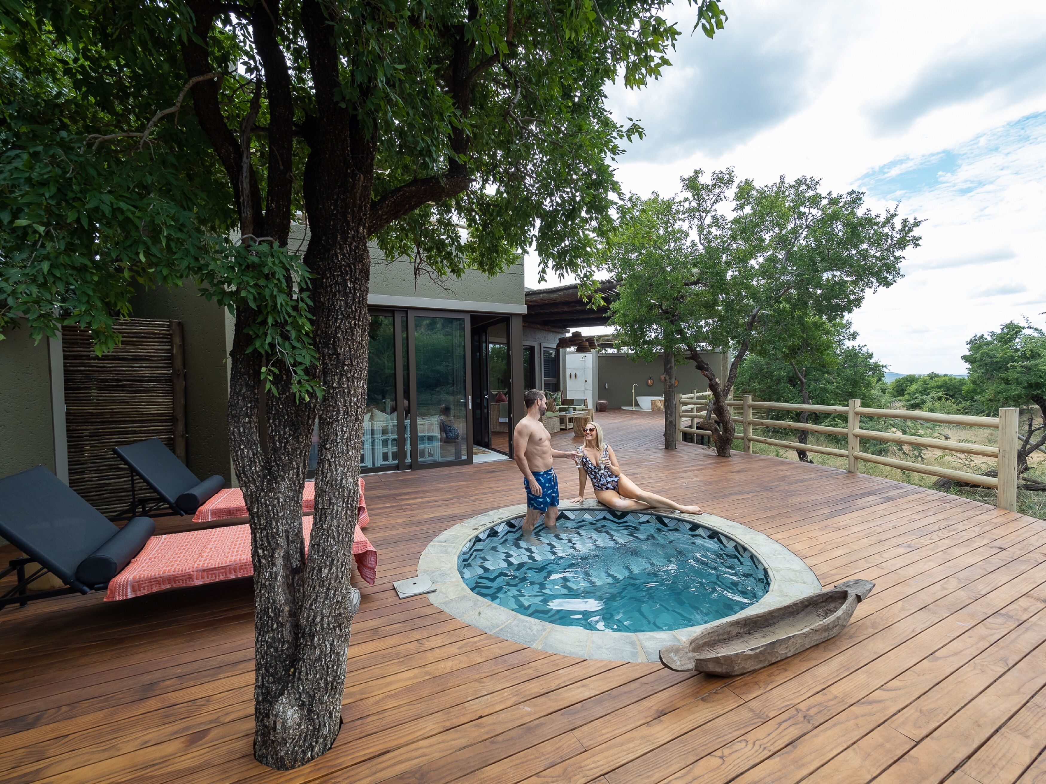 A wooden deck with a hot tub, lounge chairs, and a modern house with glass doors.