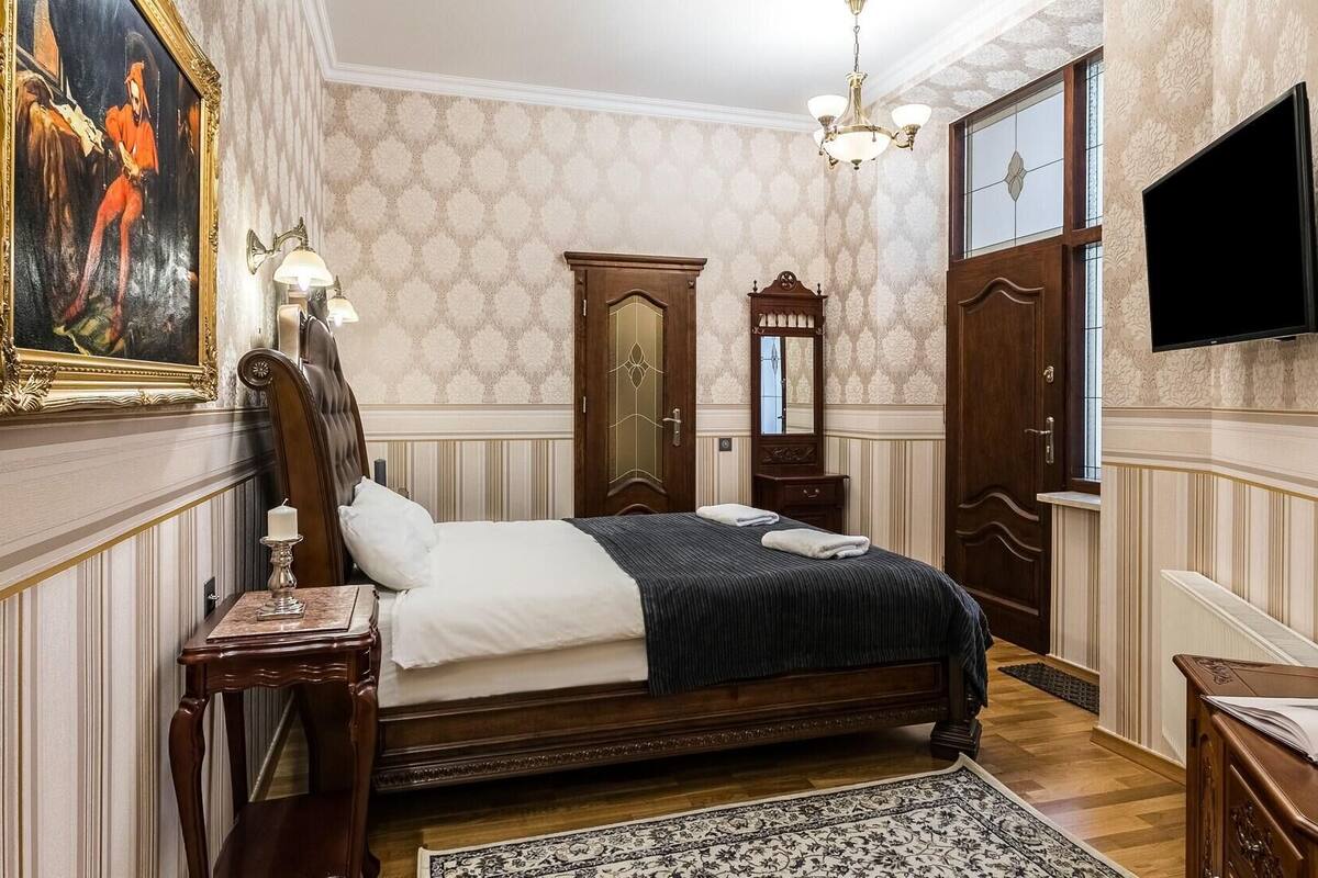 A classic bedroom with a large bed, a painting, a chandelier, and a television.