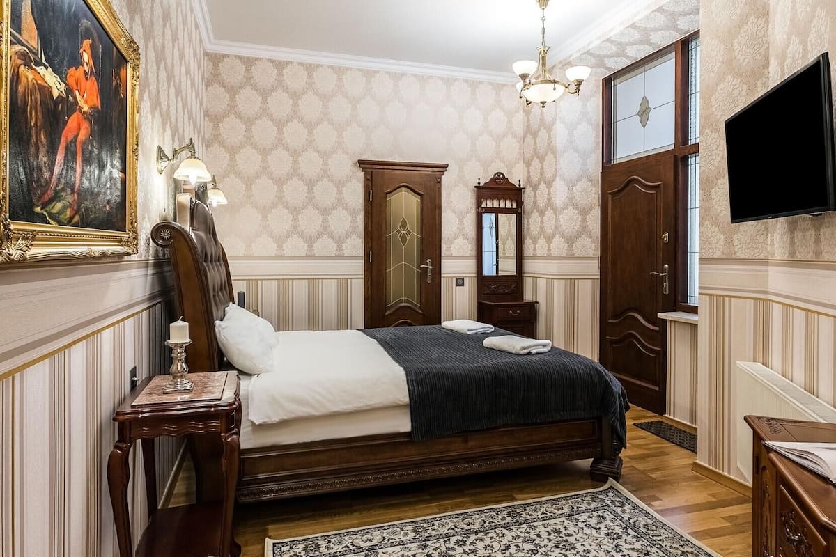 A classic bedroom with a large bed, a painting, a chandelier, and a television.