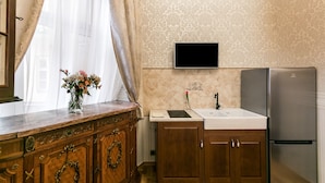 Una cocina con armarios de madera, encimera de mármol, refrigerador de acero inoxidable y televisor instalado en la pared.