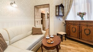 Un salón acogedor con un sofá color beige, un mueble de madera con coronas decorativas y una mesita con una taza y pasteles.