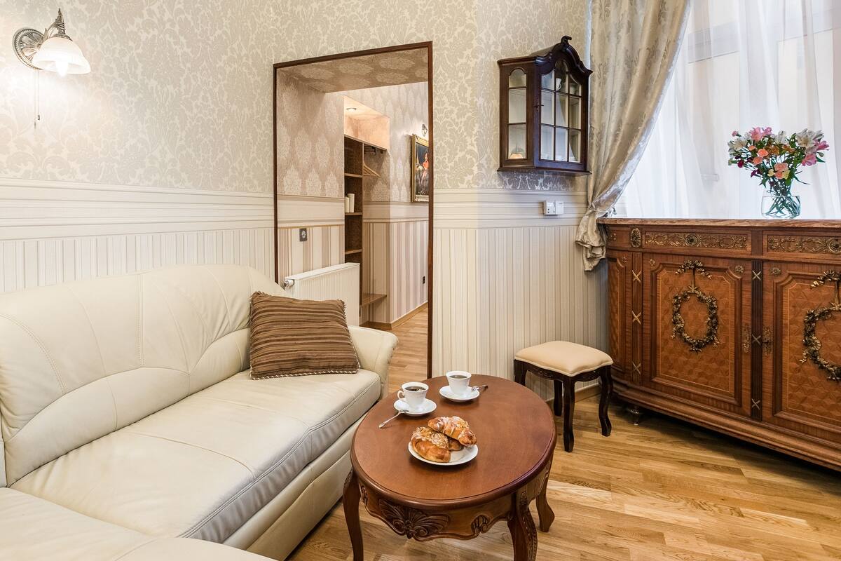 A cozy living room with a beige sofa, a wooden cabinet with decorative wreaths, and a small table with a cup and pastries.