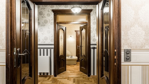 Un pasillo con puertas de madera, un radiador y una cama al fondo.