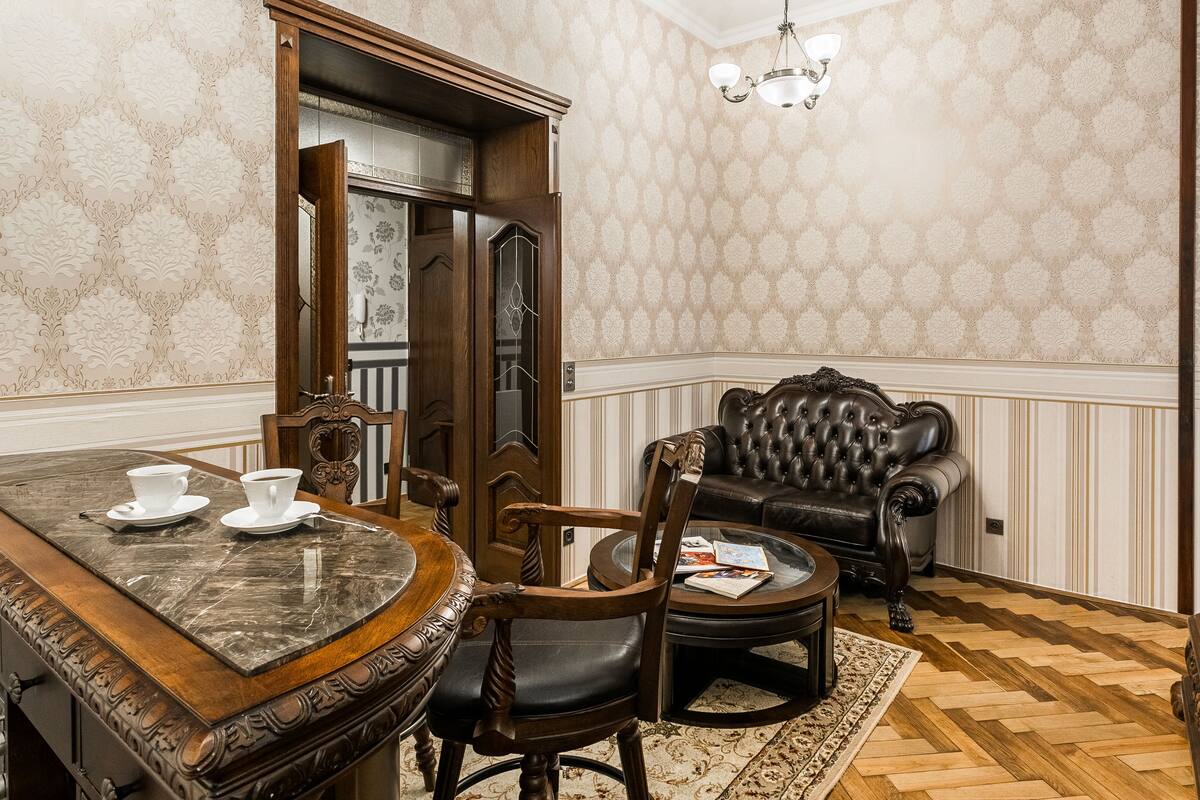 A dining area with a marble table, chairs, and a coffee cup. There is a leather sofa and a patterned rug on the floor.