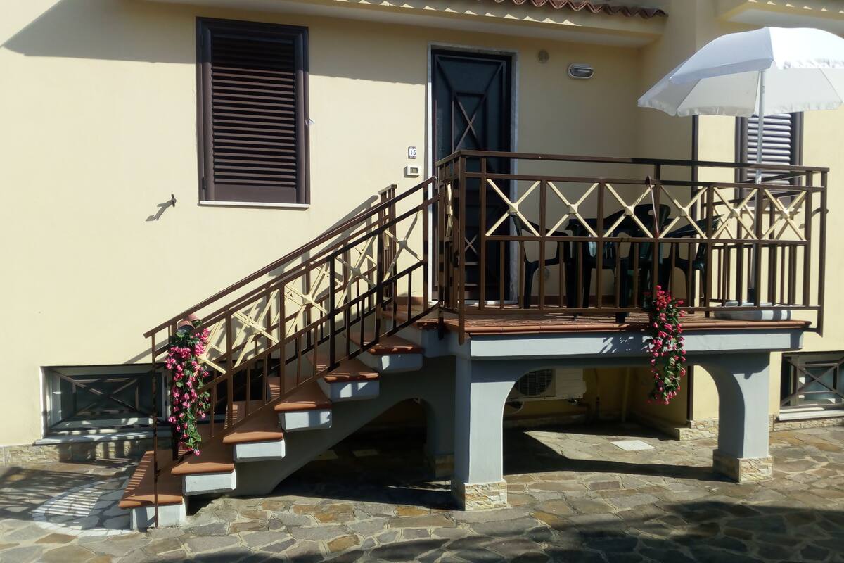 A building with a staircase leading to a balcony, stone flooring, and a white umbrella.