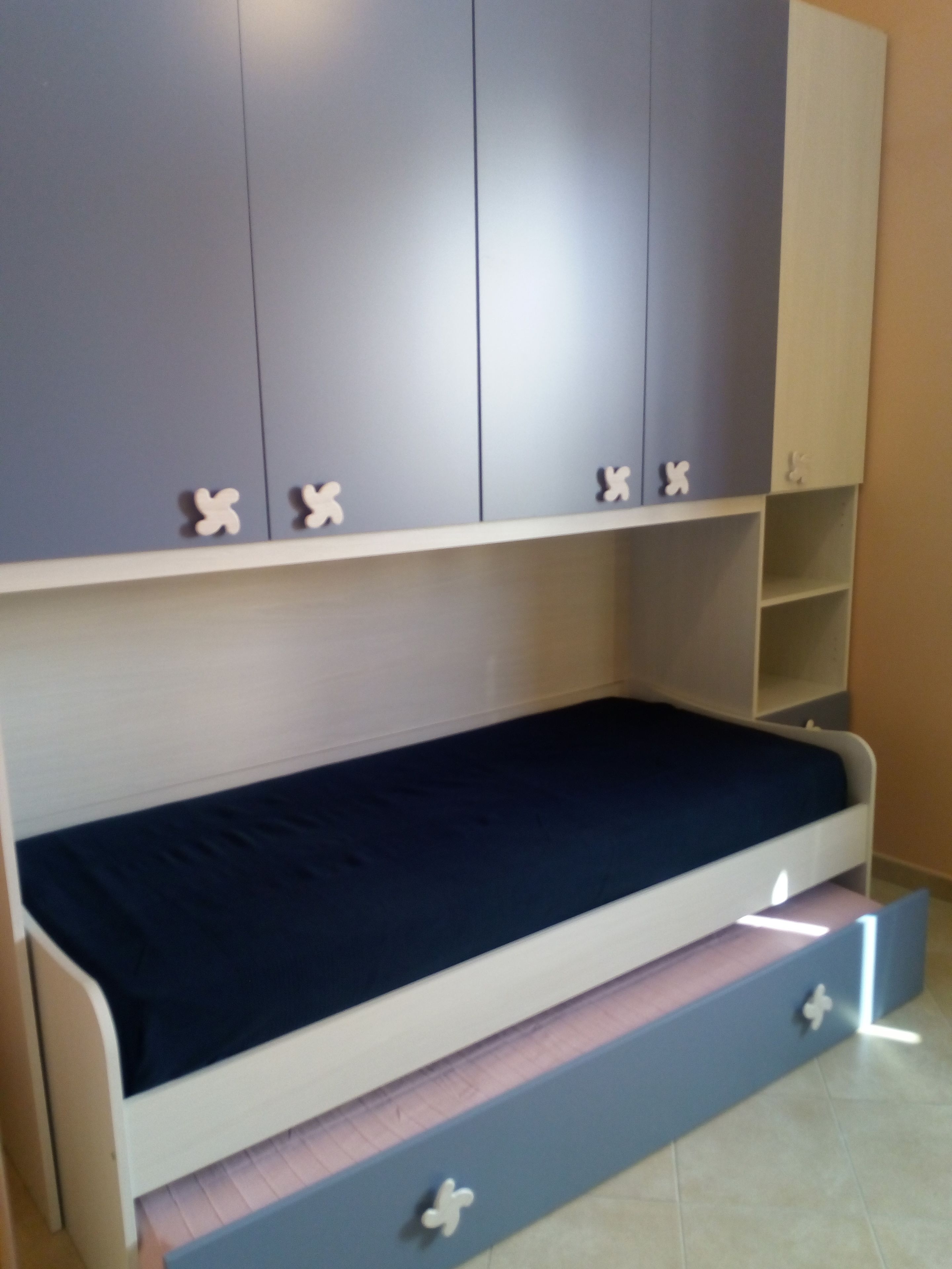 Una cama litera con un cajón en la cama inferior, un armario con espejo y una pequeña estantería.