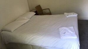 A neatly made bed with white linens, a folded towel, and a chair against the wall. - The Canberra Guest House (Wellingborough)