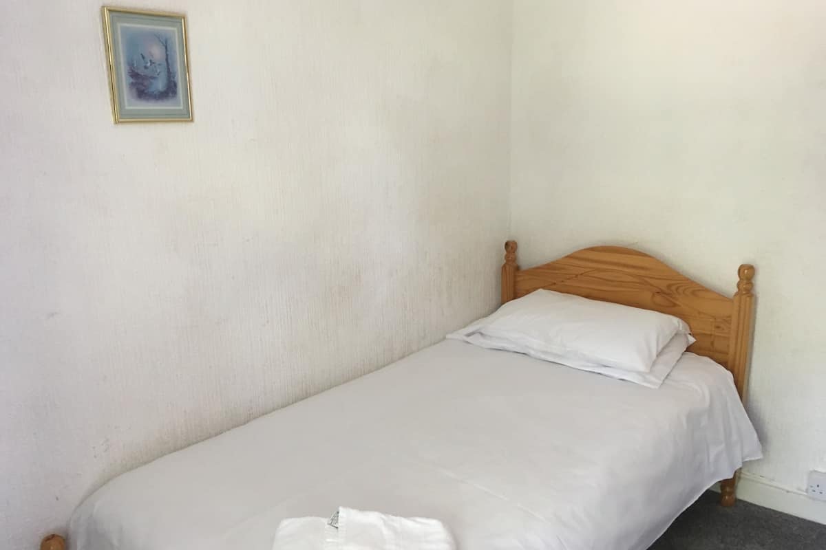 A single bed with a wooden headboard in a room with plain white walls.