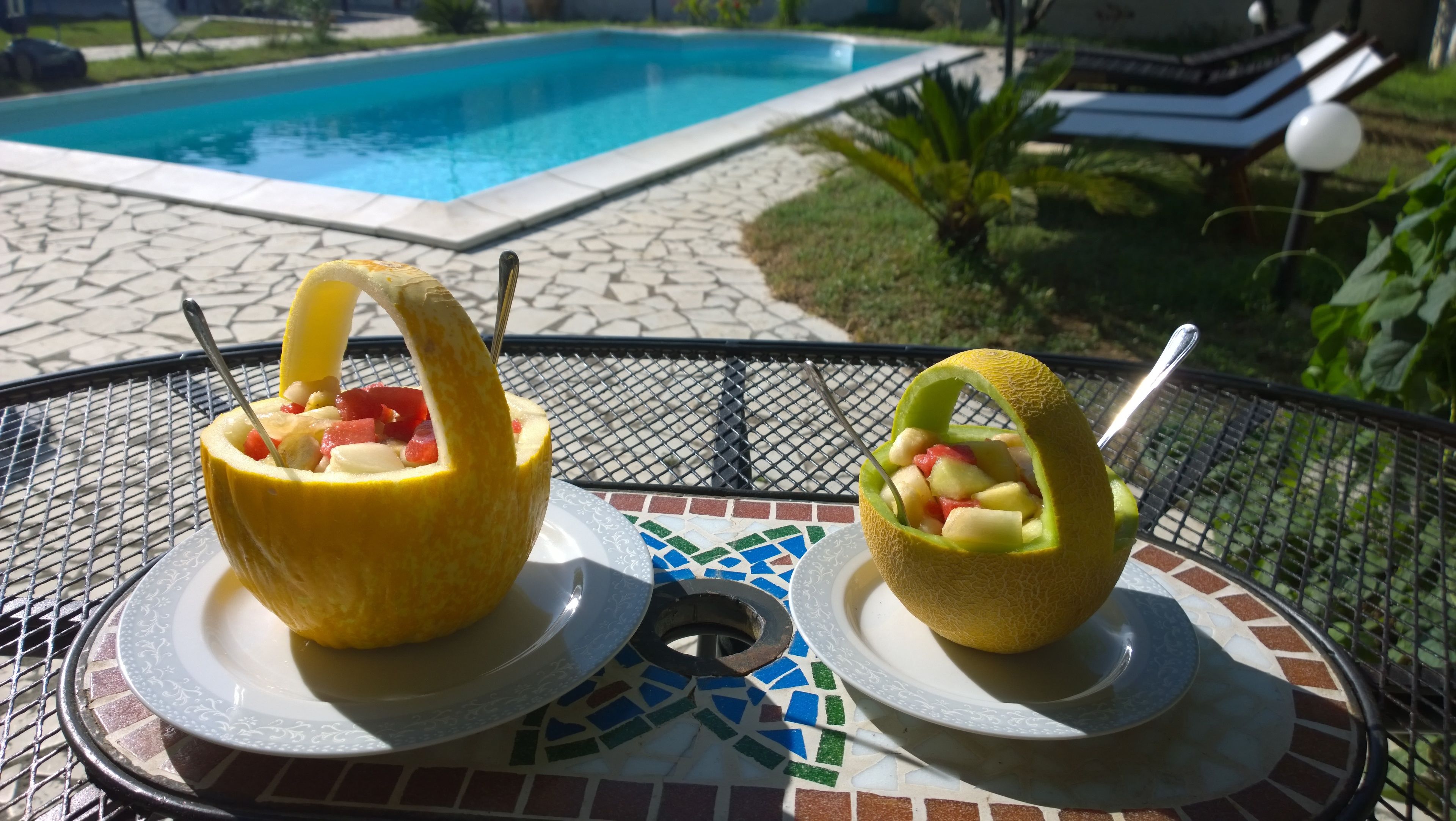 Two fruit bowls on a table with a pool in the background.