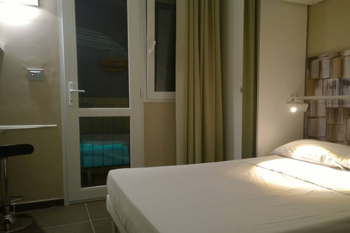 A hotel room with a bed, a chair, a window with curtains, and a wall with a patterned design.