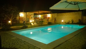 A swimming pool with a tiled deck, surrounded by a garden with a pergola and a mural on the wall. - B&B Villa Romina (Lecce)