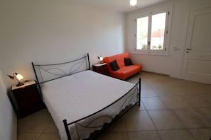 A bedroom with a bed, a nightstand, a red sofa, and a window with a view of the outside. - B&B Villa Romina (Lecce)