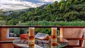 Una mesa de vidrio con dos jarras de cerveza y un libro, con vista a un paisaje verde y exuberante con árboles y colinas.