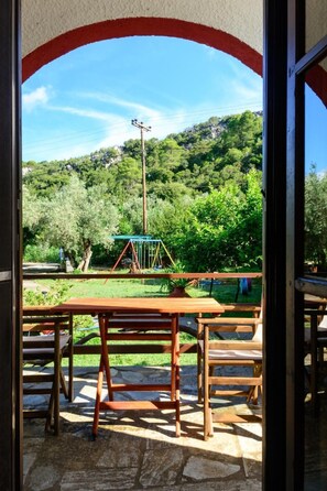 Un patio al aire libre con mesa y sillas de madera, un conjunto de columpios y vistas a una ladera verde.