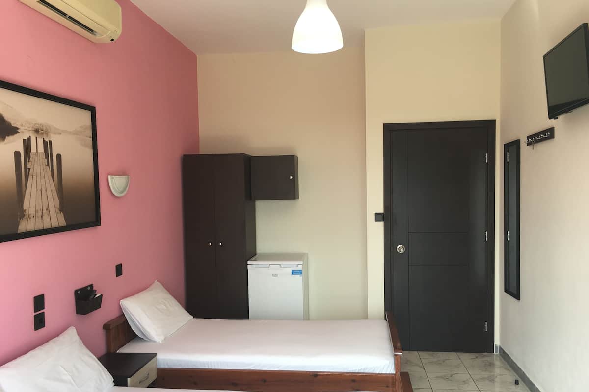 A room with two beds, a refrigerator, a wardrobe, a television, and a door.