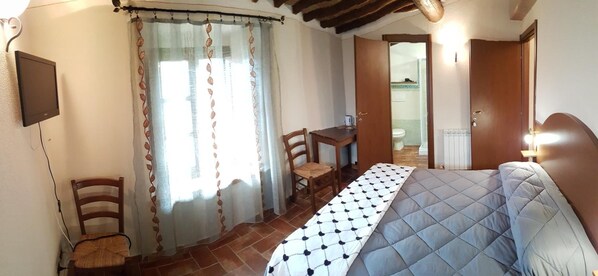 A bedroom with a bed, a desk, and a chair. There is a bathroom visible through an open door. - Il Pozzo di Sant'Andrea (Siena)